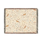 A beige woven cotton blanket with a floral and bird pattern, featuring a colorful fringed edge.