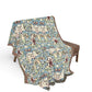 Decorative blanket with leaf pattern draped over a chair on a white background