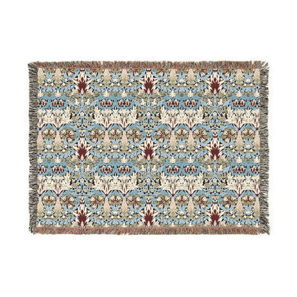 A woven blanket with a floral pattern in shades of blue, beige, and red with a fringed edge.