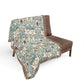 Beige patterned throw blanket draped over a brown chair on a white background