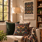 A styled living room scene featuring a William Morris & Co. botanical and bird patterned throw pillow, a matching patterned throw blanket draped over a beige sofa, and a dark green velvet pillow.