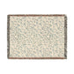 A rectangular woven cotton blanket with a floral pattern in subtle colors, featuring a colorful fringed edge.