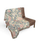 Floral patterned throw blanket draped over a brown chair on a white background