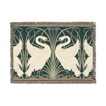 A woven cotton blanket with a geometric William Morris & Co pattern featuring swan motifs in a white and green colour scheme with colourful fringed edges.
