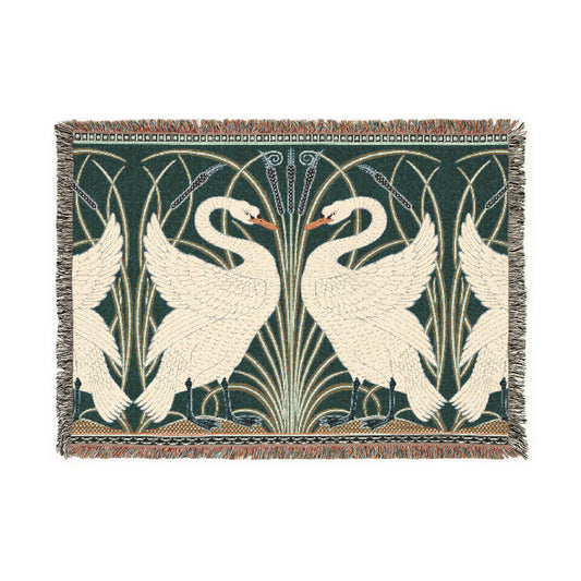 A woven cotton blanket with a geometric William Morris & Co pattern featuring swan motifs in a white and green colour scheme with colourful fringed edges.