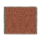 A woven cotton blanket with a geometric pattern in a rust color, featuring a colorful fringed edge.