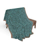 Green patterned blanket draped over a brown chair on a white background