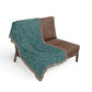 Teal patterned throw blanket draped over a brown chair on a white background