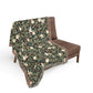 Green patterned blanket draped over a brown chair on a white background
