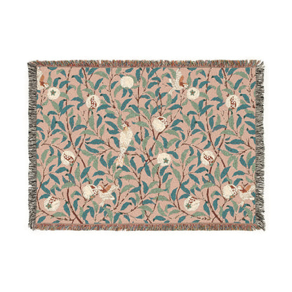 A woven cotton blanket with a floral William Morris & Co pattern in shades of green and beige, featuring birds and pomegranate motifs, with a colourful fringed edge.