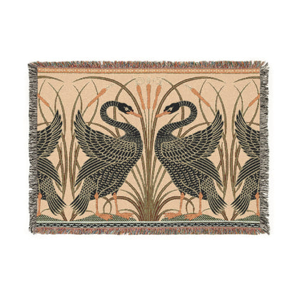 A woven cotton blanket with a geometric William Morris & Co pattern featuring birds, in beige, black, and green colours, with fringed edges.