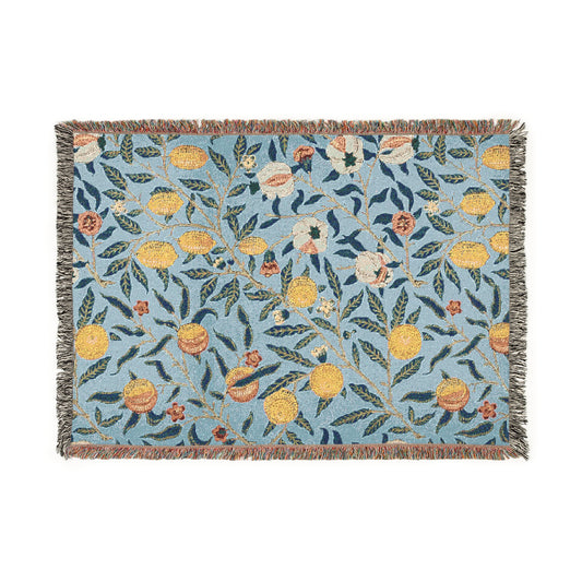 A woven cotton blanket with a floral William Morris & Co pattern in shades of blue and yellow, featuring colourful fruit motifs and a fringed edge.
