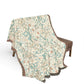 A woven throw blanket with a detailed botanical and bird pattern draped over a brown armchair against a solid white background.