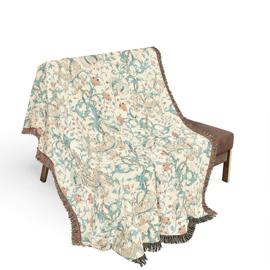 A woven throw blanket with a detailed botanical and bird pattern draped over a brown armchair against a solid white background.