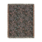 A rectangular woven throw blanket with fringe on all sides, featuring an abstract floral and vine pattern in muted pink, teal, and gray on a dark charcoal background.