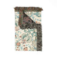 A folded woven throw blanket with a cream background, teal and rust floral scroll pattern, and dark charcoal fringe, shown on a plain white background.