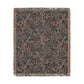 A rectangular woven throw blanket with a dark charcoal background and an intricate floral and vine pattern in dusty pink, muted teal, and light gray, finished with fringed edges.