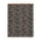 A rectangular woven throw blanket with fringed edges, featuring an abstract pattern in dusty pink, teal blue, and light gray on a dark charcoal background.