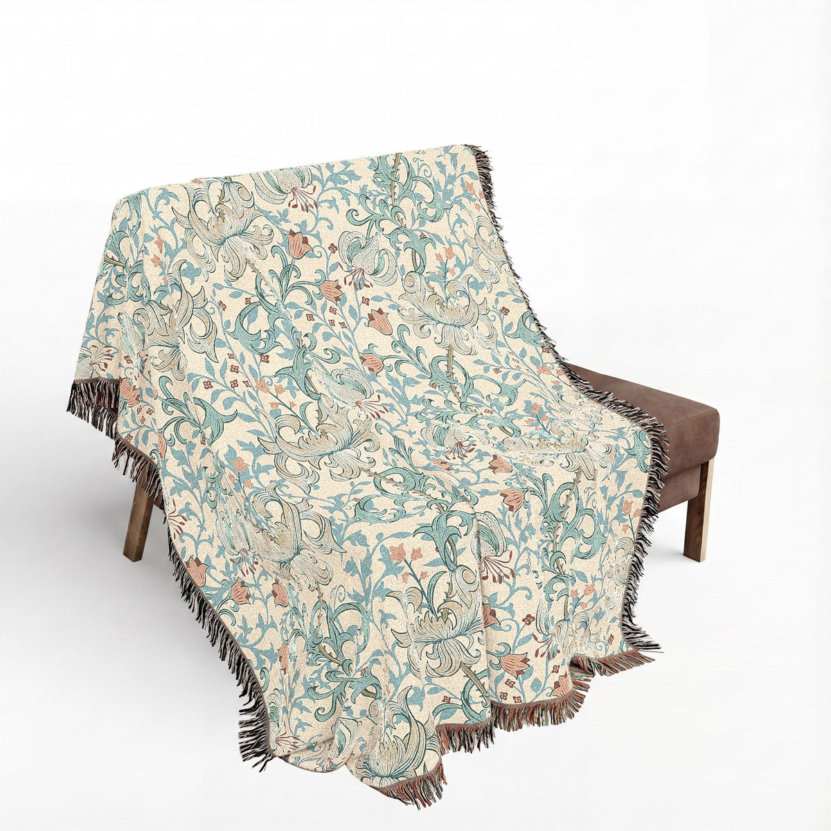 A woven throw blanket with a detailed botanical and animal pattern in muted teal, beige, and brown, draped over a brown armchair against a plain white background.
