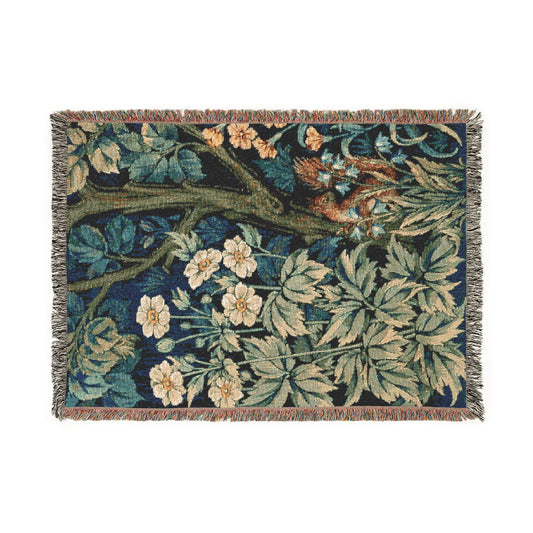 A woven cotton blanket with a nature-inspired geometric pattern featuring squirrels and flowers, predominantly in green and brown tones, with a colourful fringed edge.