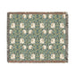 A woven cotton blanket with a green and floral pattern, featuring a colorful fringed edge.