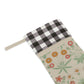 A Christmas stocking with a floral William Morris & Co pattern in red and green colours, featuring a red and black checkered cuff at the top.