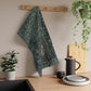A kitchen tea towel featuring an artistic design with green foliage and a fox among the leaves.