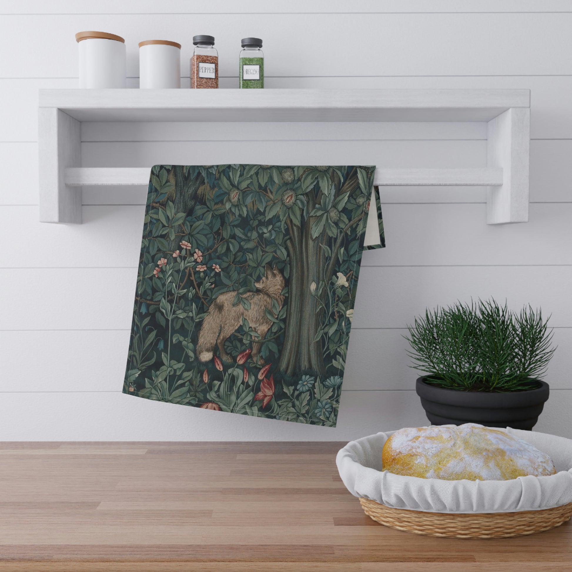 A kitchen tea towel featuring an artistic design with green foliage and a fox among the leaves.