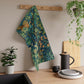 A kitchen tea towel featuring an artistic design with pheasants, squirrels, and floral elements on a blue background.