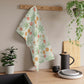 A kitchen tea towel featuring a floral William Morris & Co pattern with prominent orange and green colours on a white background.