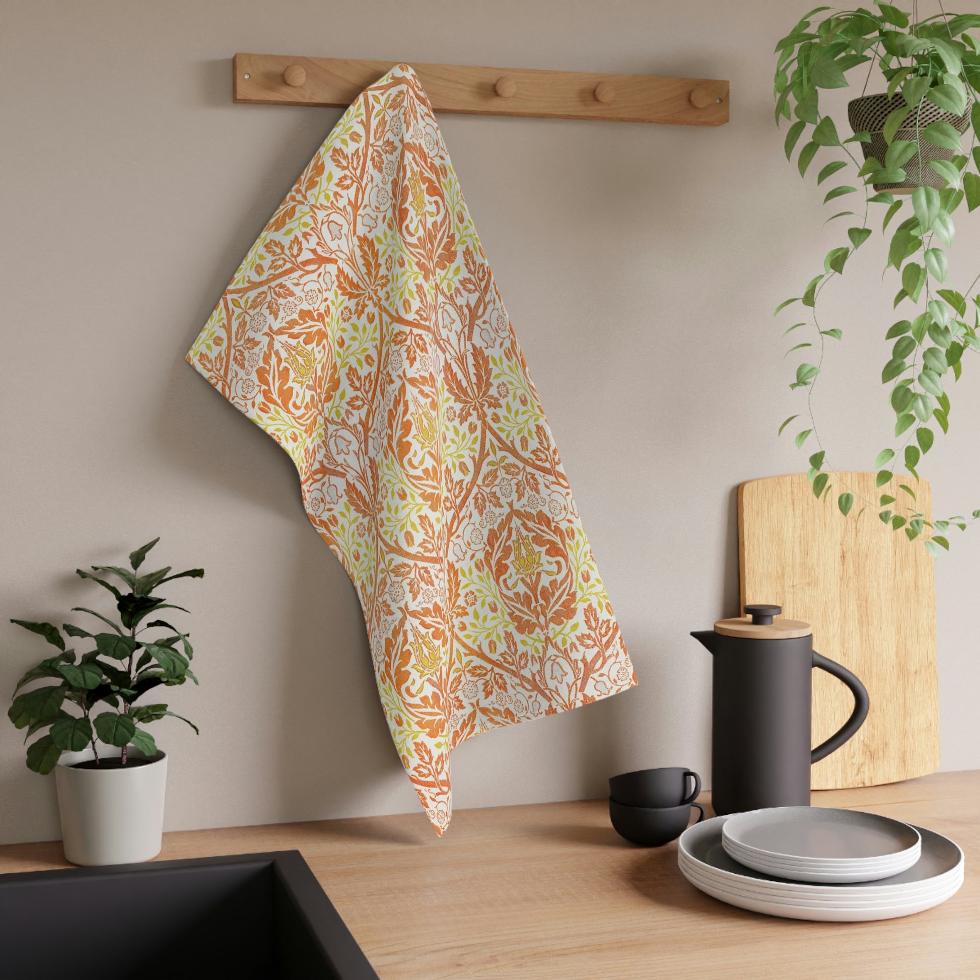 A kitchen tea towel with a floral William Morris  & Co pattern in orange, green, and yellow colours on a light background. 