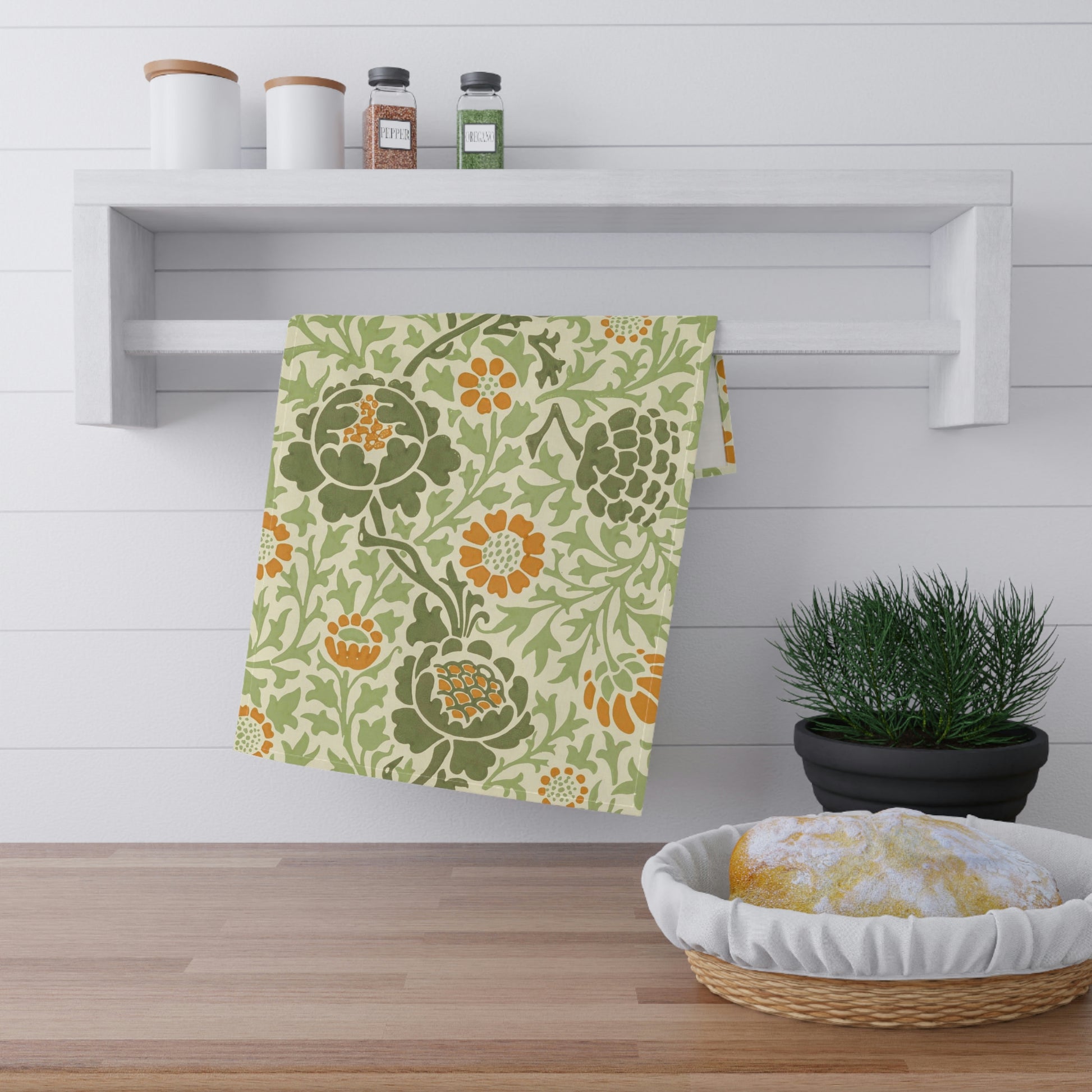 A kitchen tea towel with a floral William Morris & Co pattern featuring green, orange and yellow colours on a light background.