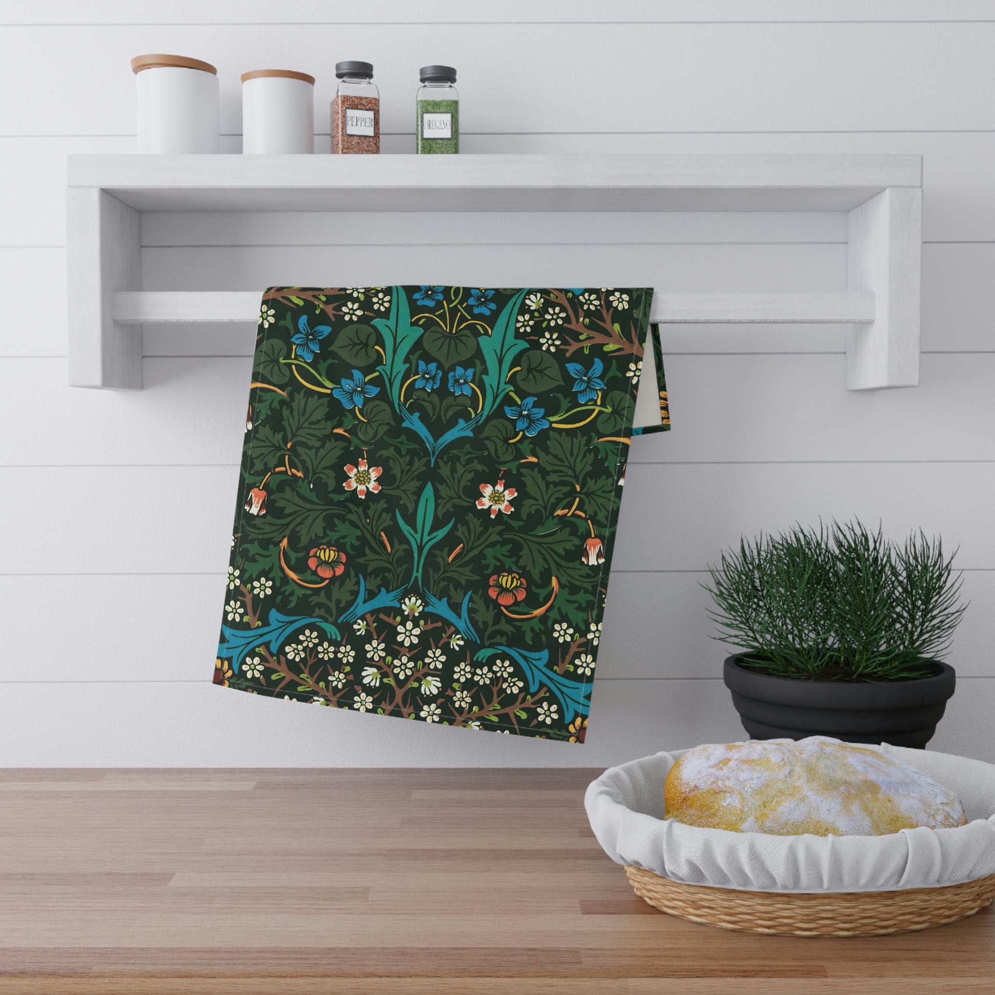 A kitchen tea towel with a floral pattern inspired by William Morris, featuring tulips in red and blue on a dark green background.