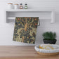 A kitchen tea towel featuring an artistic William Morris & Co design with birds, flowers, and leaves on a green background.