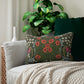 A rectangular lumbar cushion with a floral William Morris & Co pattern featuring predominantly green, with accents of red, yellow and blue.
