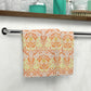 A white washcloth with a geometric floral pattern inspired by William Morris, featuring orange and yellow colors.