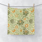 A white washcloth with a floral pattern inspired by William Morris, featuring green and orange colours.