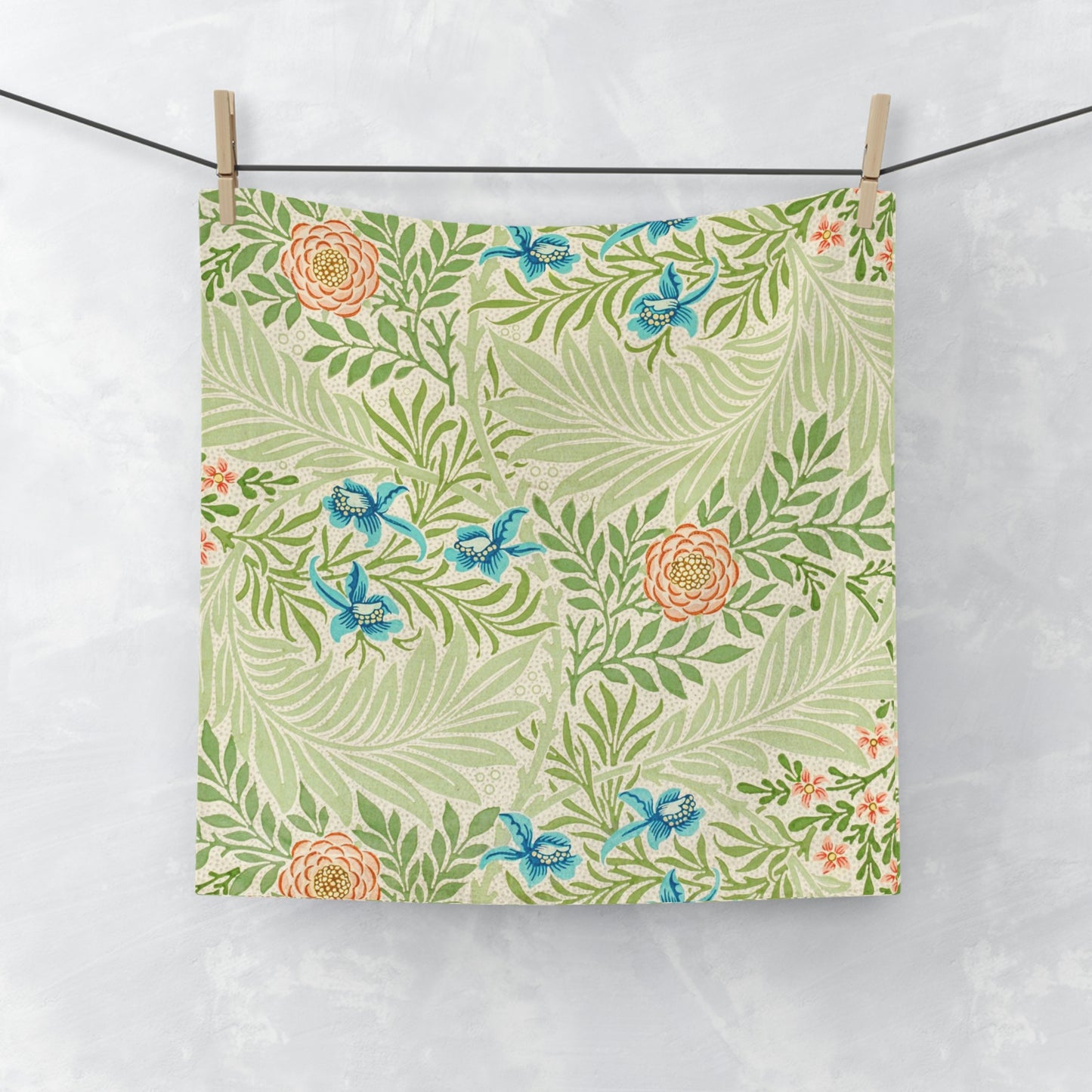 A white washcloth with a floral pattern inspired by William Morris, featuring green leaves and blue flowers.