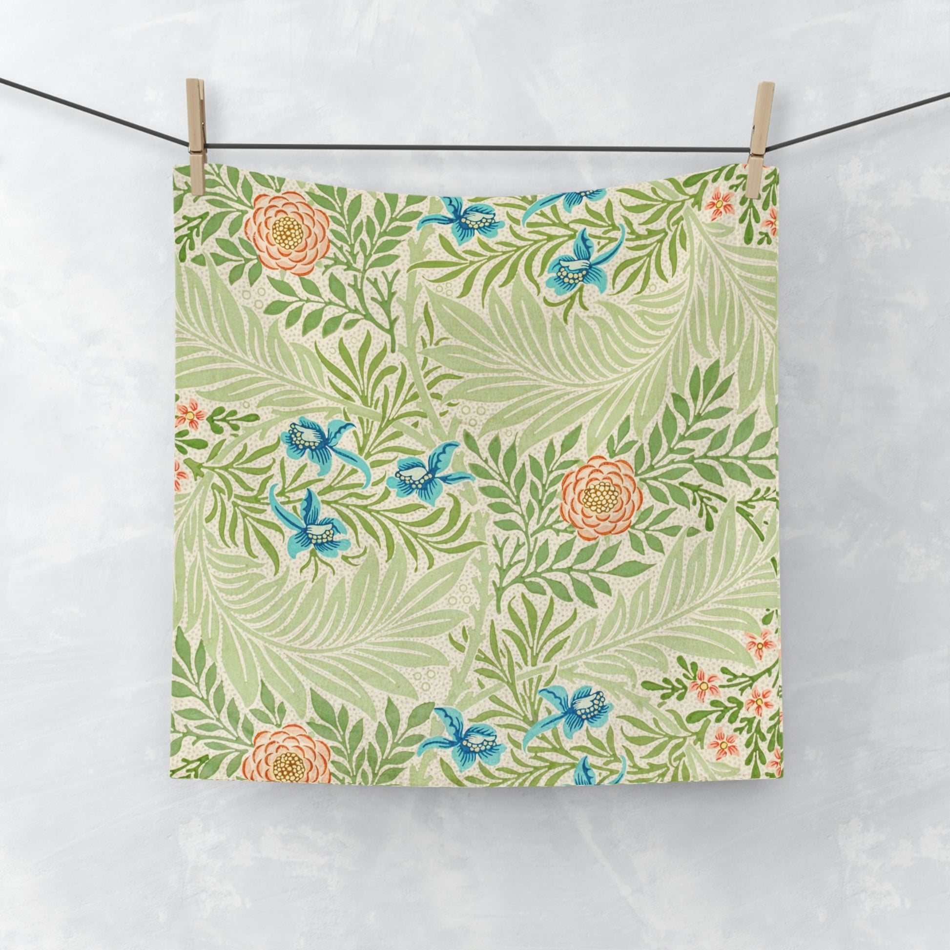 A white washcloth with a floral pattern inspired by William Morris, featuring green leaves and blue flowers.