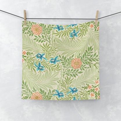 A white washcloth with a floral pattern inspired by William Morris, featuring green leaves and blue flowers.