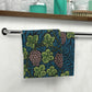 A white washcloth with a floral pattern inspired by William Morris, featuring green leaves and pink grapes.